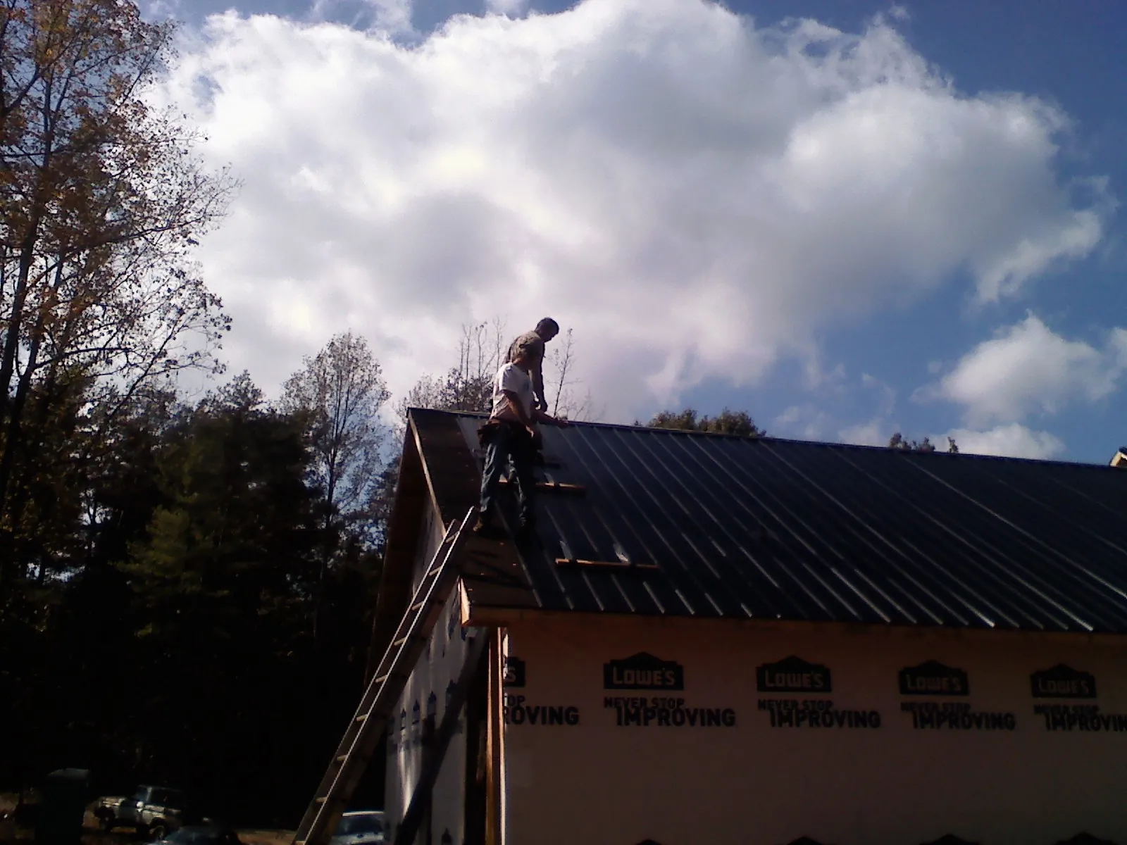Roofer fastening dark metal panels high against a cloudy sky, from a Roof Inspection job in Essex