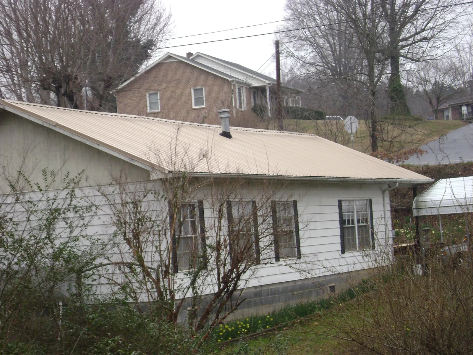 Tan metal roof on a white sided house set into a hillside — Commercial Roofing by Roofing Brothers in Essex